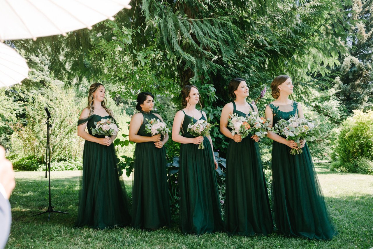  Bridesmaids in green dresses look on to ceremony 