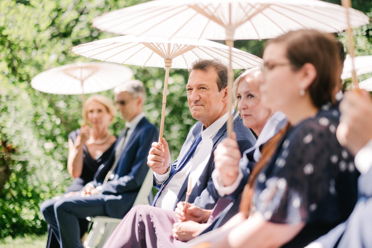  Father and mother of bride look on under umbrellas during readings 