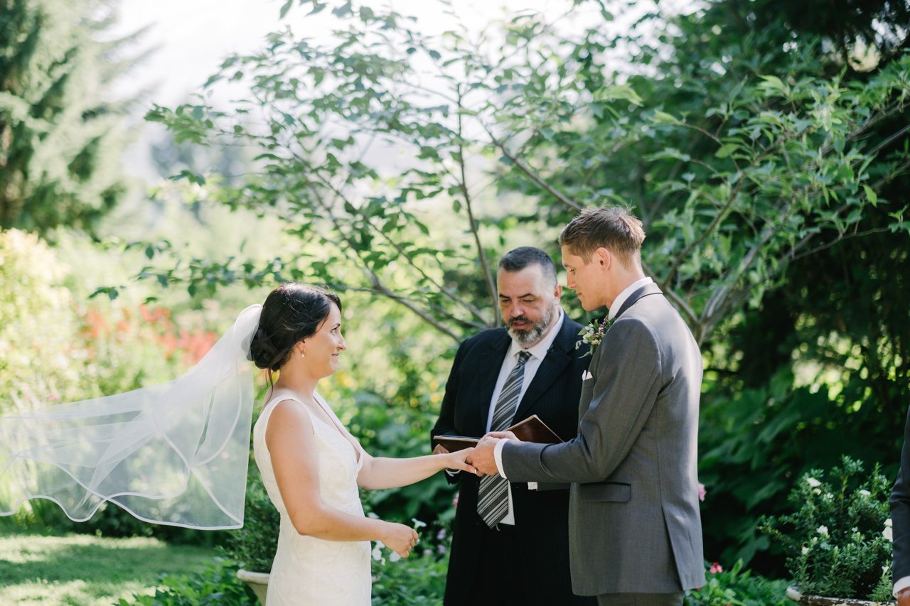  Groom places ring on brides finger while veil blows 