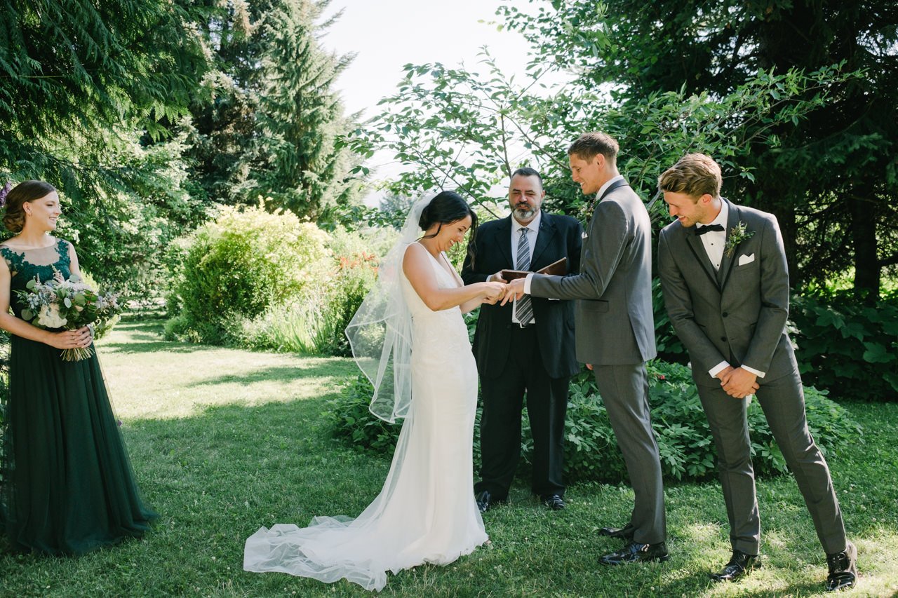 Bride forces ring onto groom's finger while best man looks on closely 