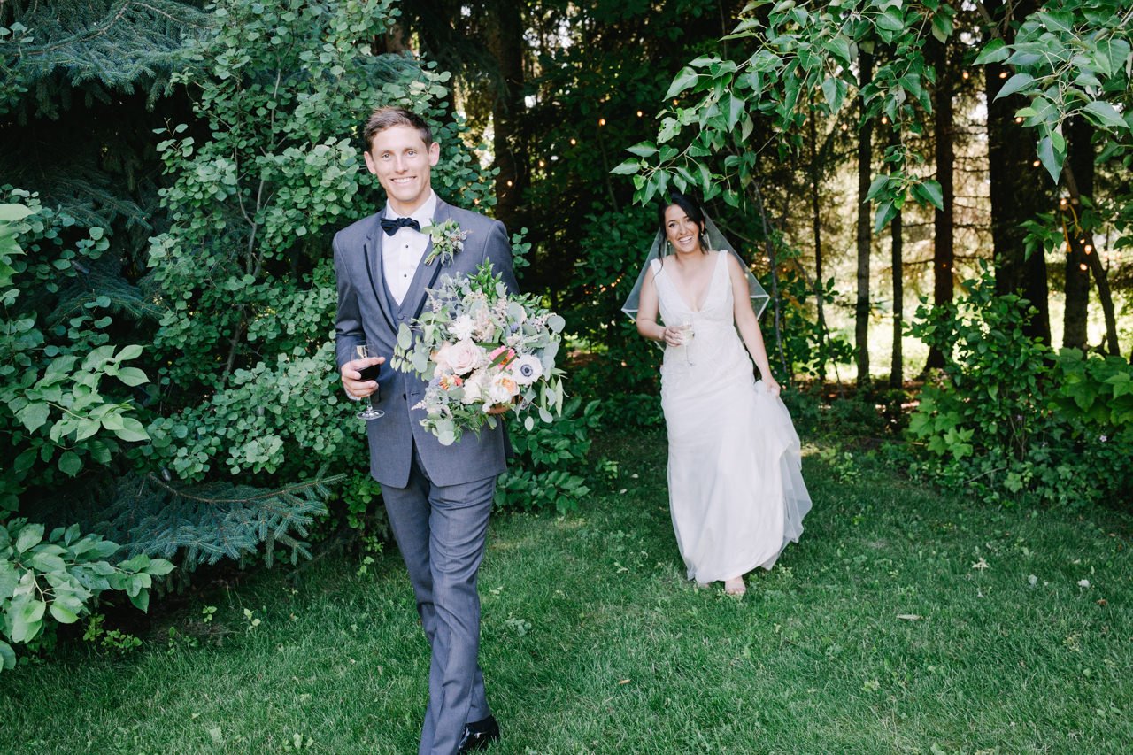  Bride and groom return out of trees to reception with glasses of wine 