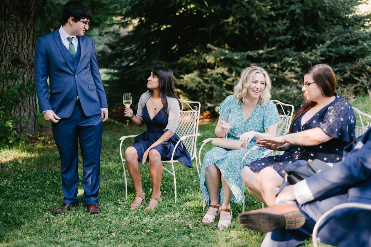  Wedding guests sitting in white wire chairs laughing together 