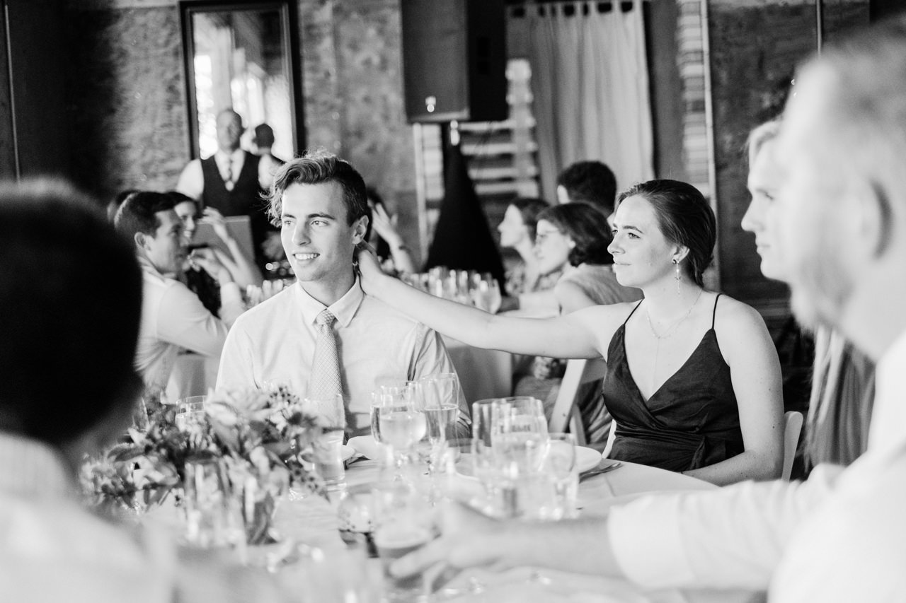  Black and white photo of wedding guests with girl scratching boyfriends head 