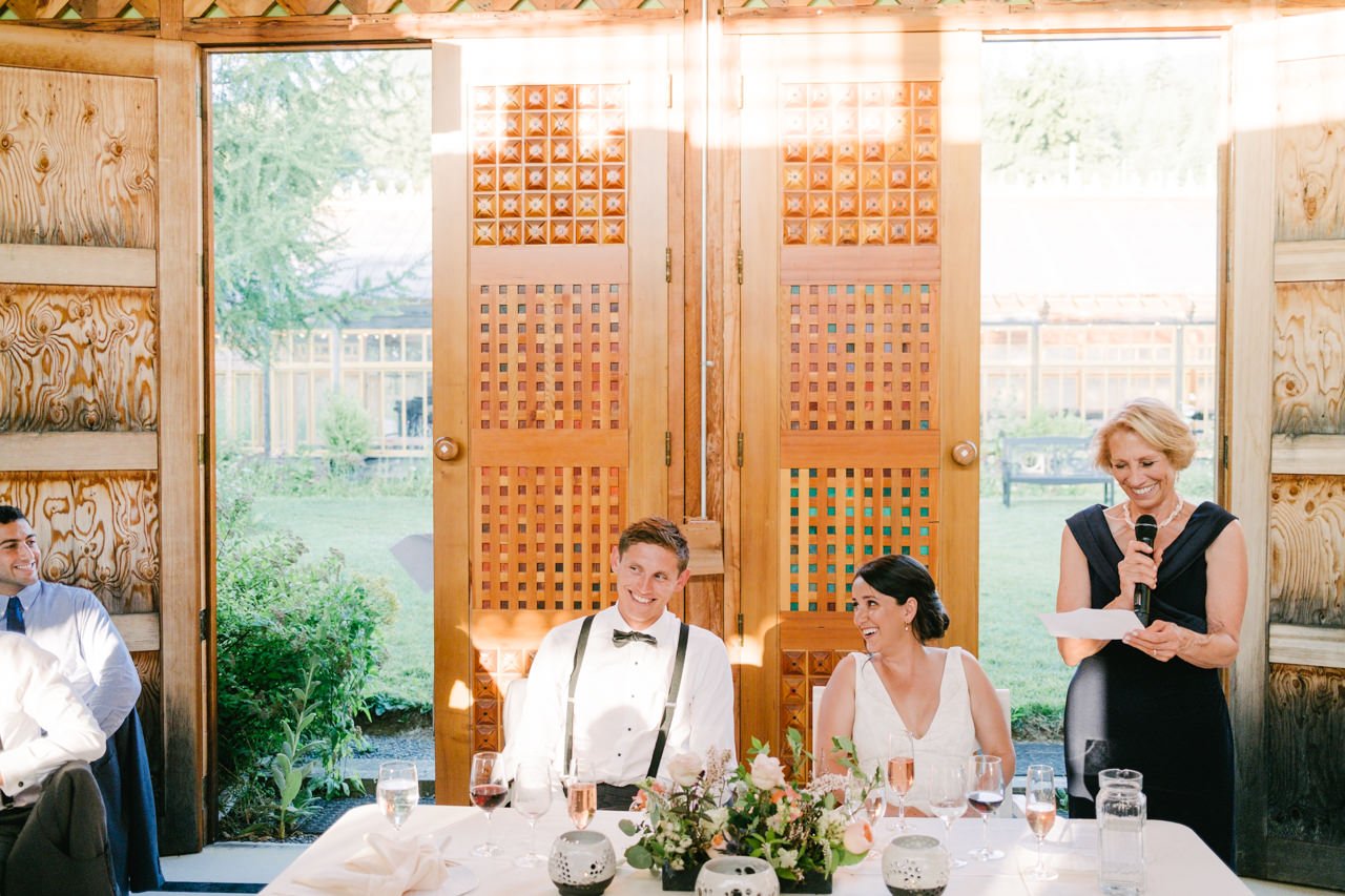  Couple laughs during toast by mother of groom in front of wooden doors 