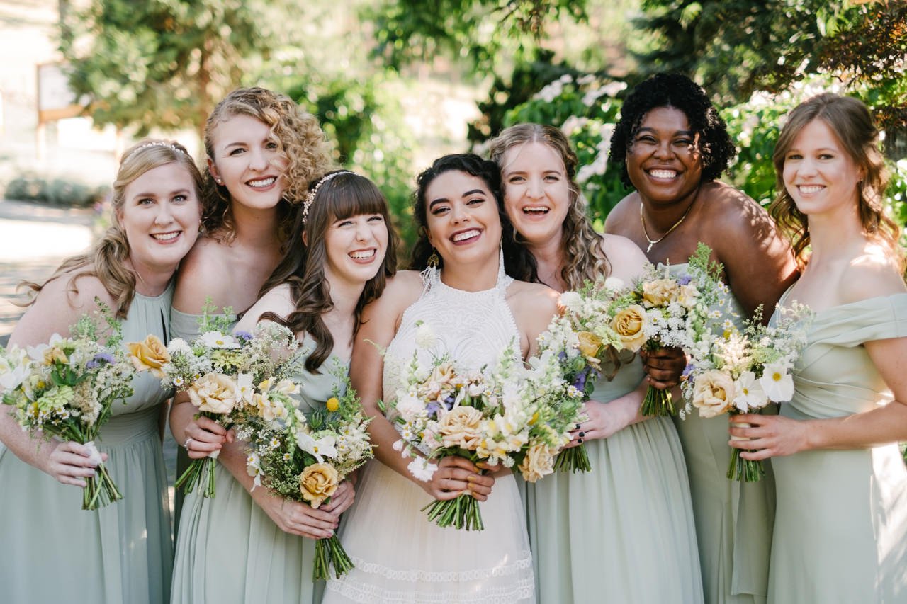  Bridesmaids in light green dresses and white and yellow bouquets smile with bride 