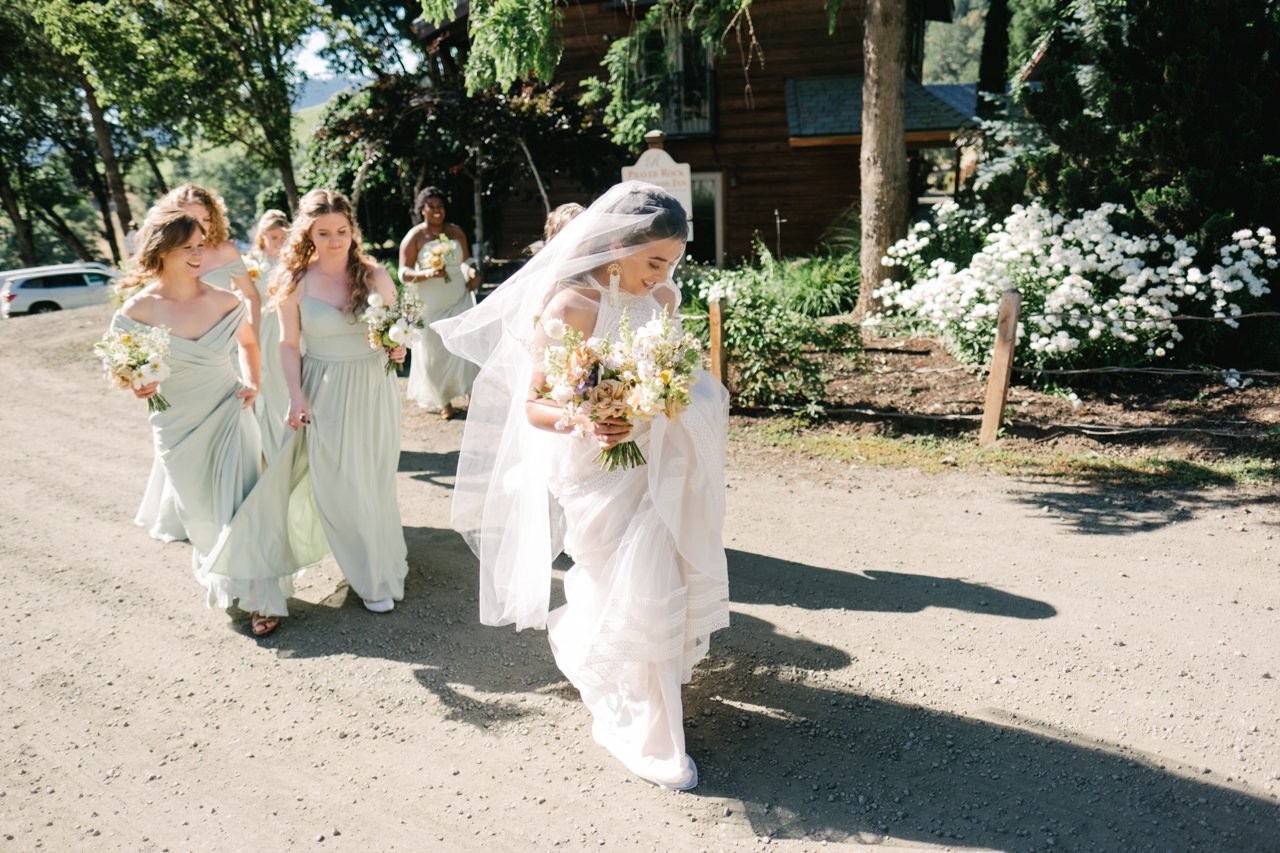  Bride covered in veil walks with bridesmaids in light green dresses to the ceremony 