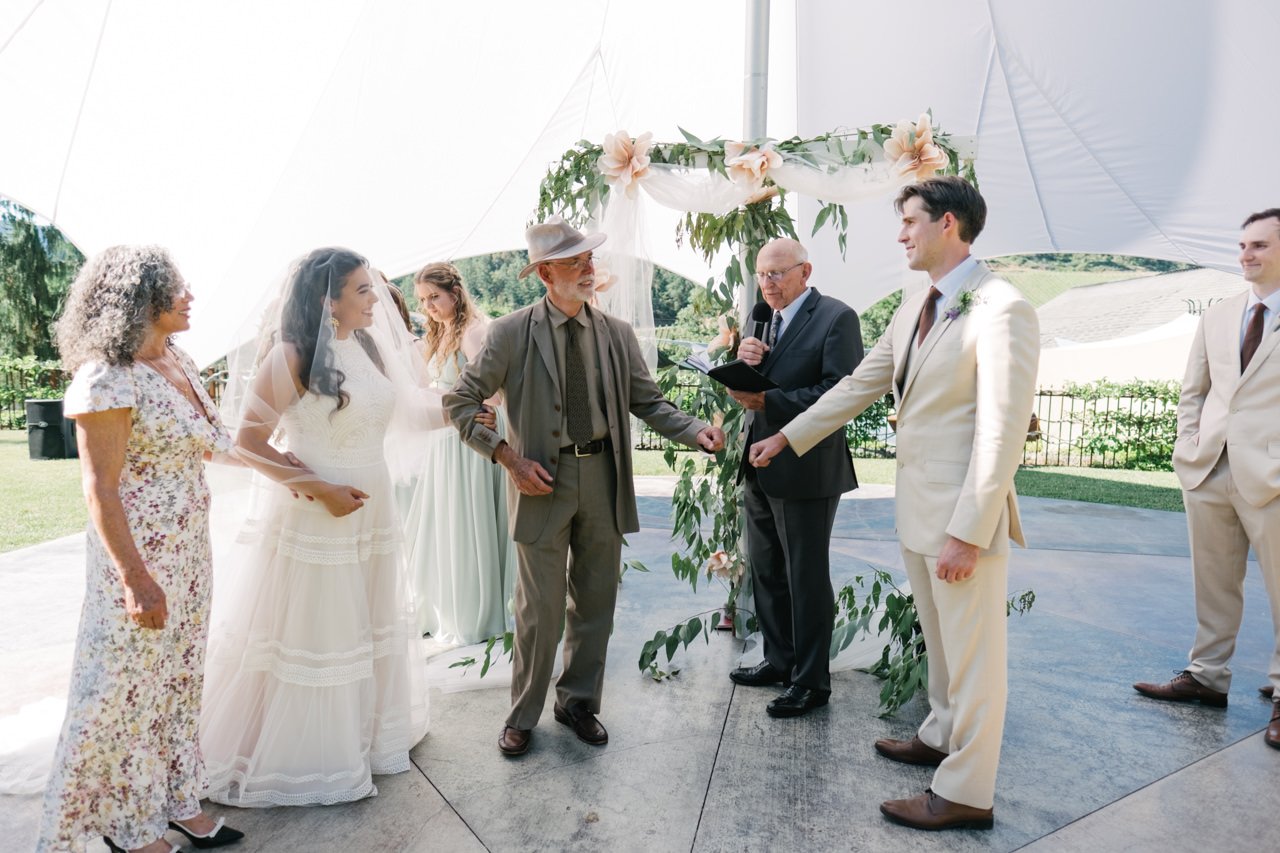  Groom and father of bride fist bump as they greet each other in front of floral backdrop 