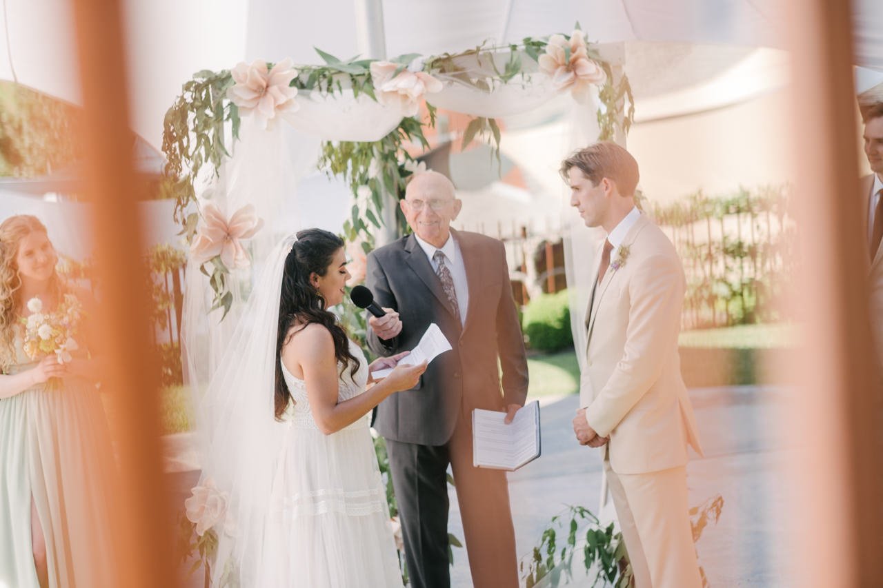  Bride reads vows under floral backdrop through rusty bars 