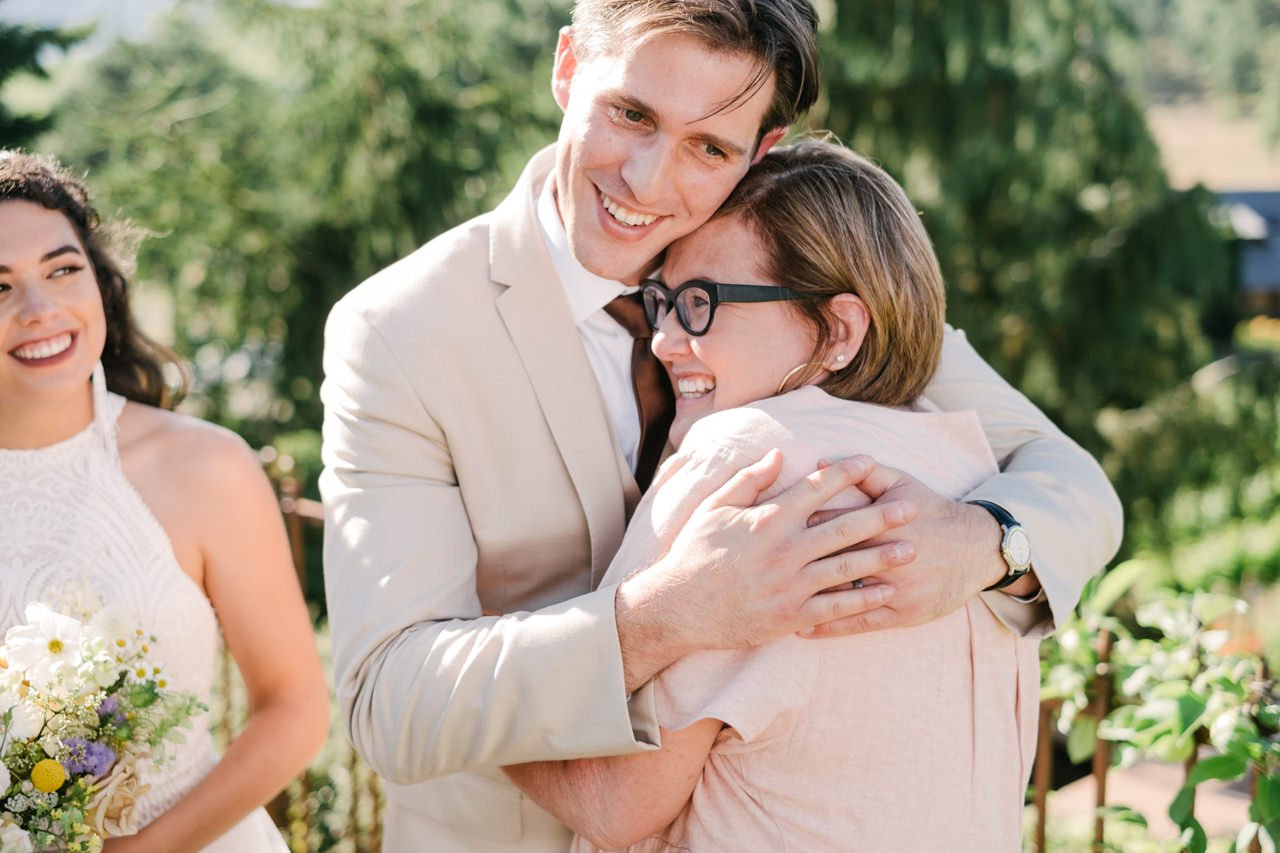  Groom in tan suit hugs aunt after wedding 