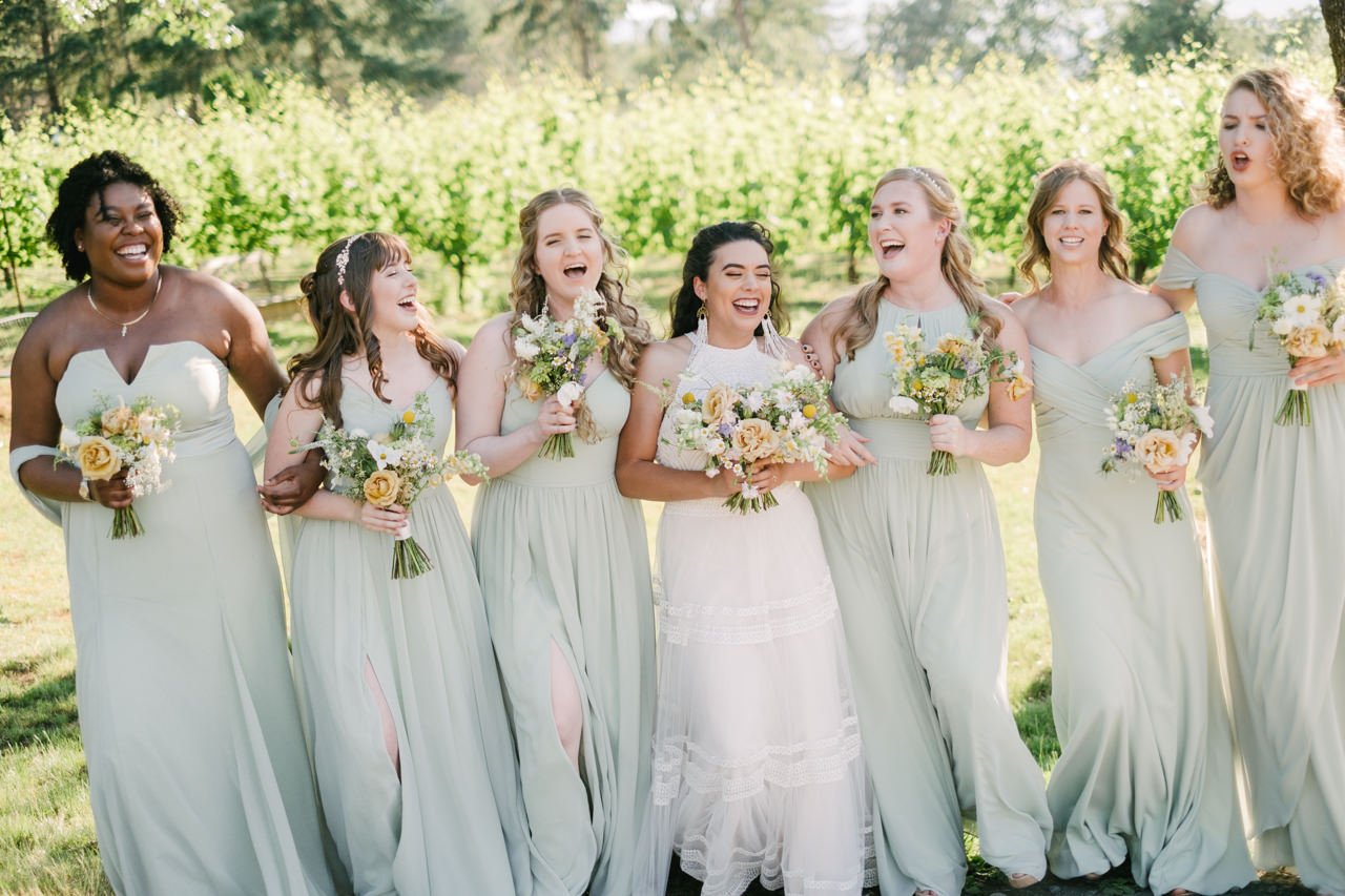  Bridesmaids laughing in light green laughing with orange and yellow bouquets 