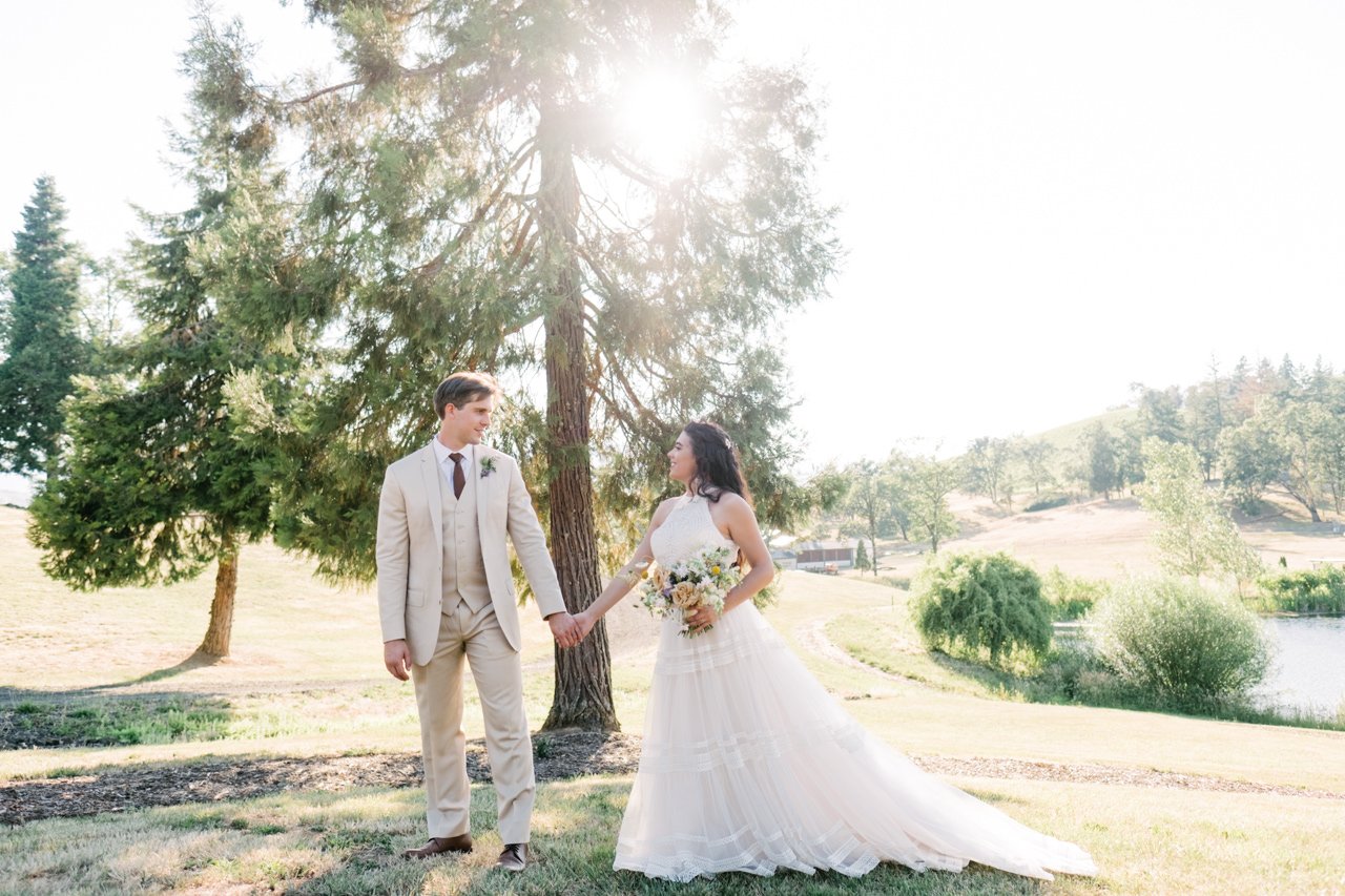  Sunlight shines through pine tree in Roseburg with bride and groom in tan suit 