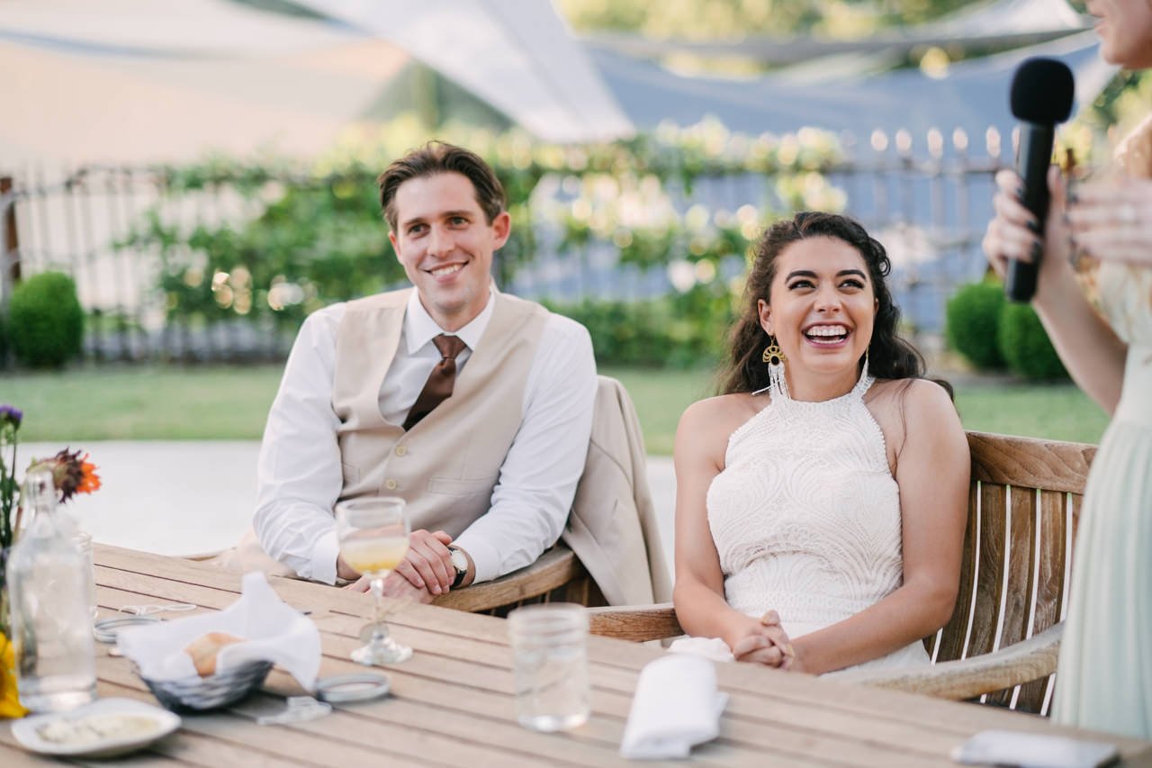  Bride and groom giggle during outdoor summer toasts 