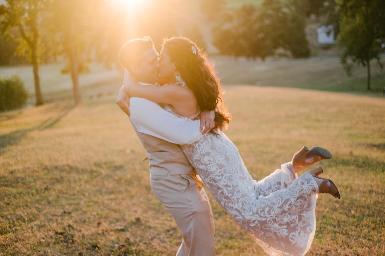  Groom twirls bride around emerged in golden hour light in farm pasture 