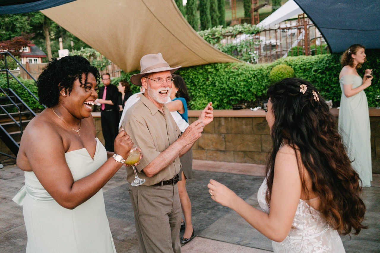  Father of bride, bridesmaid and bride laughing while dancing together under shades 