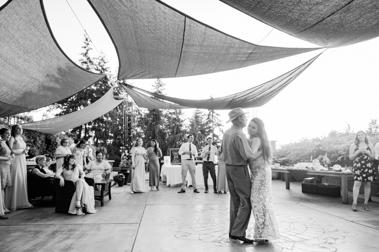  Bride dances with father wearing brim hat while guests watch under shade canopy 