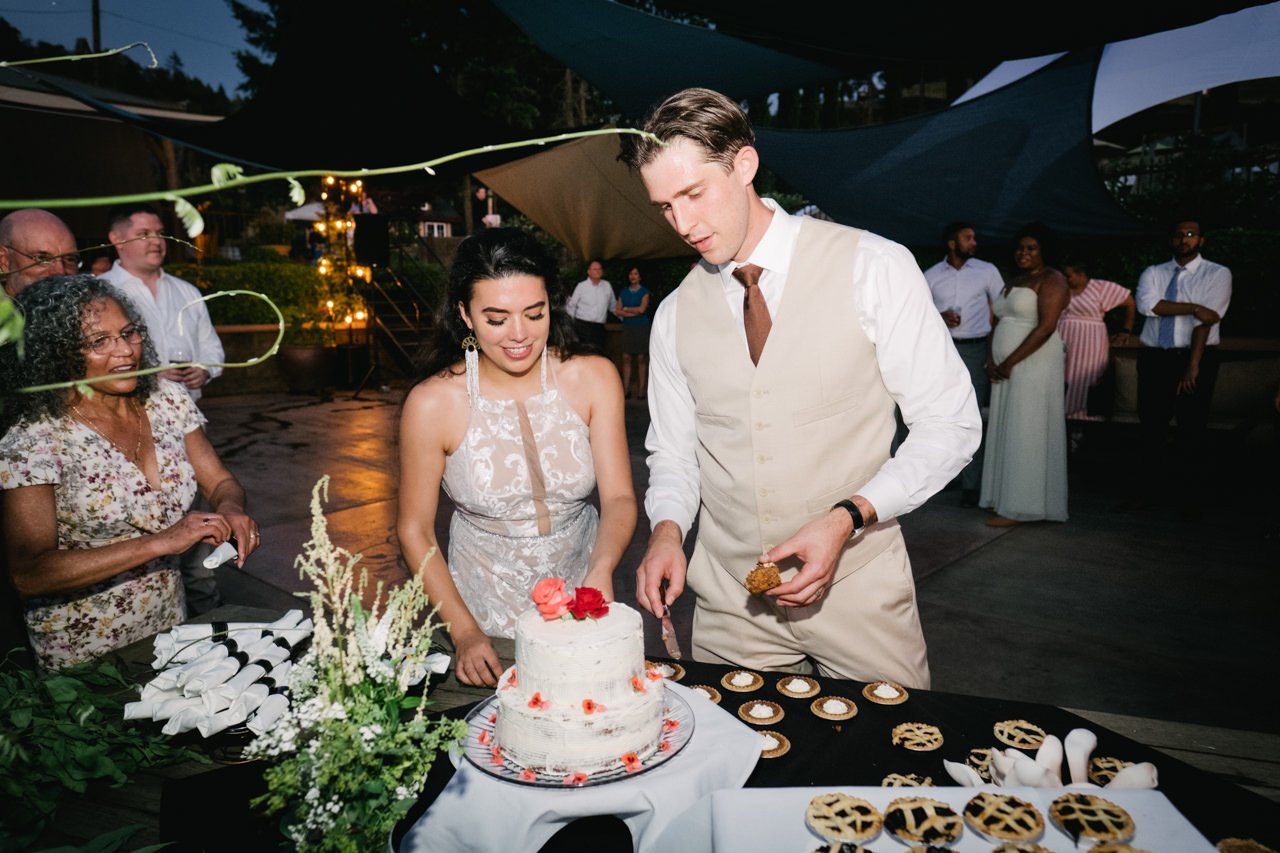  Bride and groom stand at desert table in front of pies and cake 