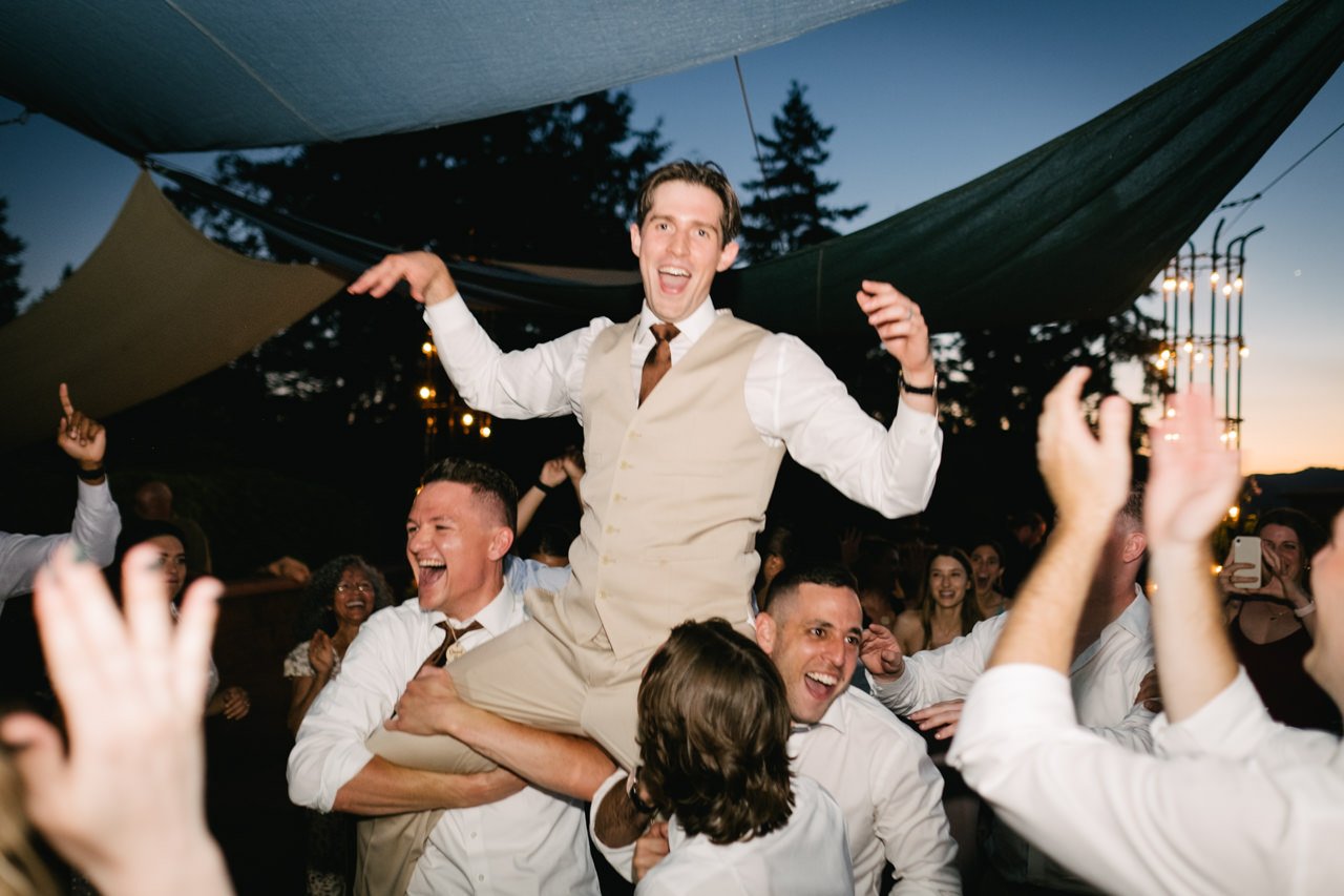  Groom hoisted on shoulders of wedding guests during evening light hour dance party 