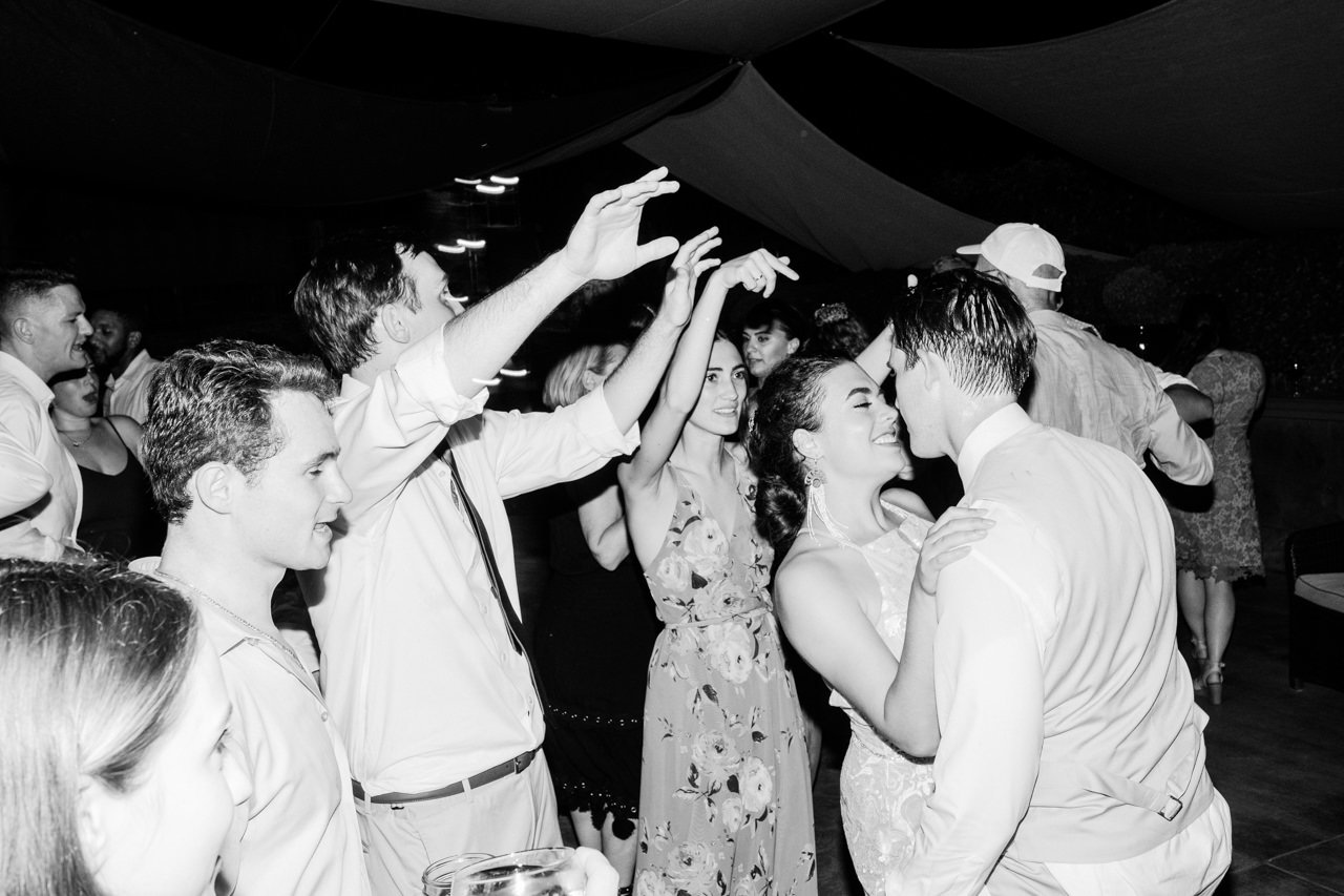  Sweaty groom hugs bride during reception with guests cheering 