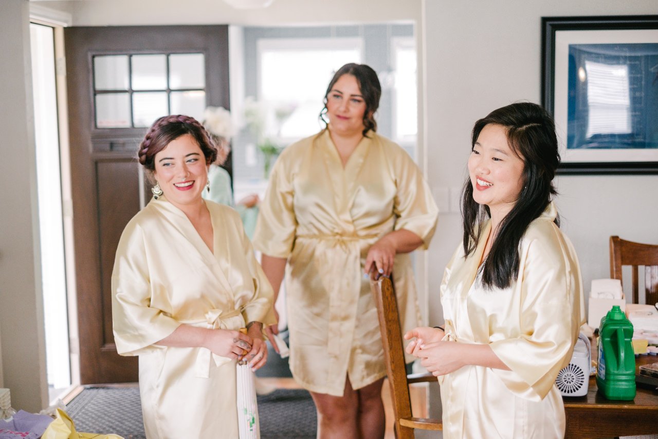  Bridesmaids in gold bathrobes smile while watching bride get ready 