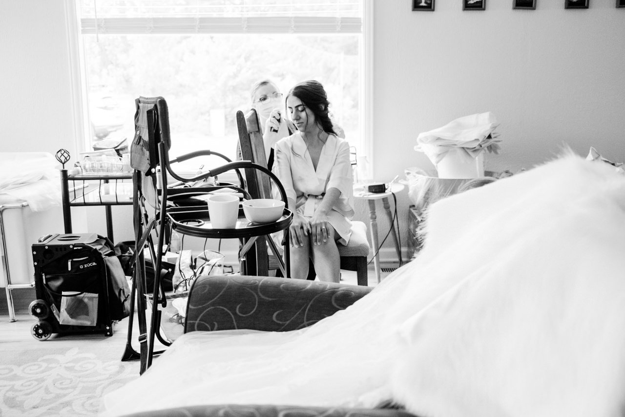  Bride sits in cluttered room while getting hair prepared 