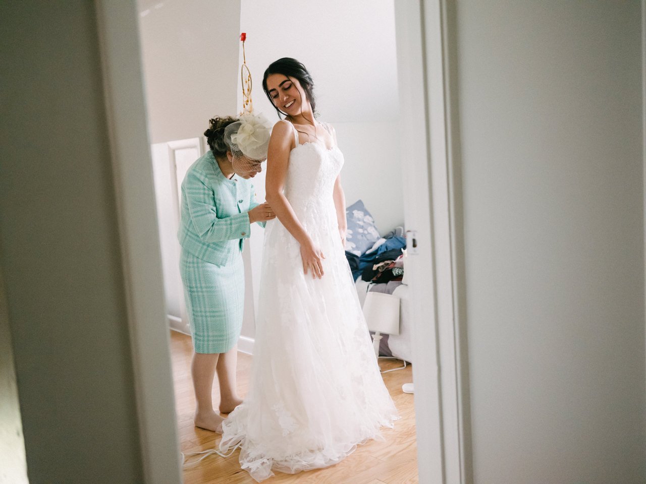  Mother of bride in teal outfit laces up wedding dress through doorway 