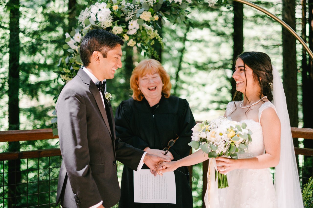  Bride and groom smiling holding hands on redwood deck 