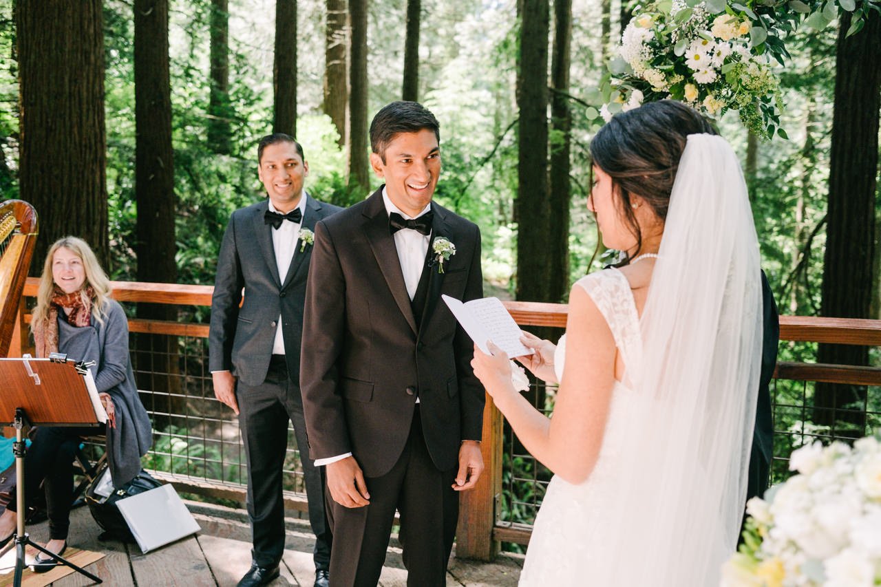  Groom with tuxedo smiles at bride's vows on redwood deck 