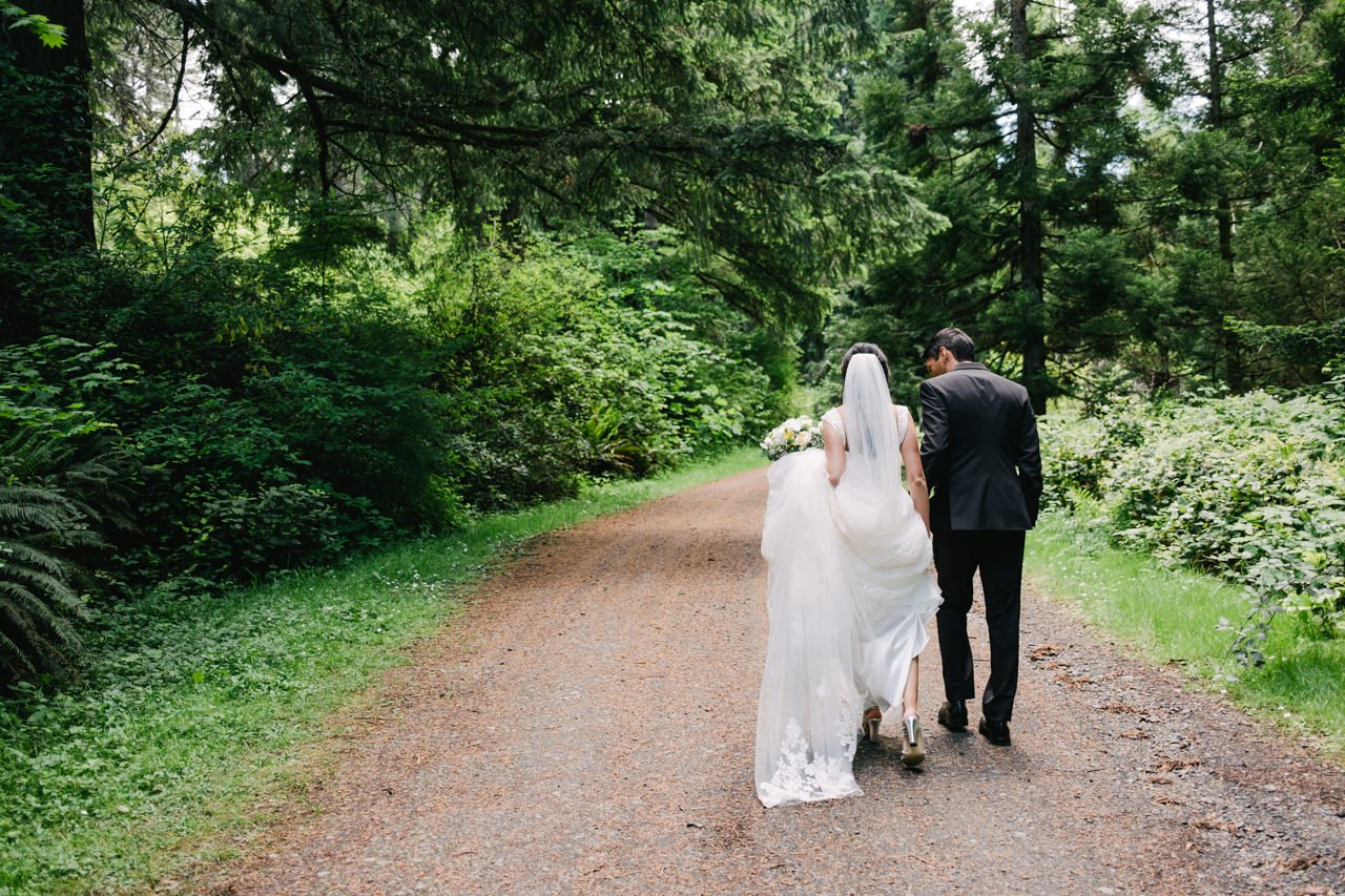  Bride and groom walk together down dirt forest road in Portland Oregon 