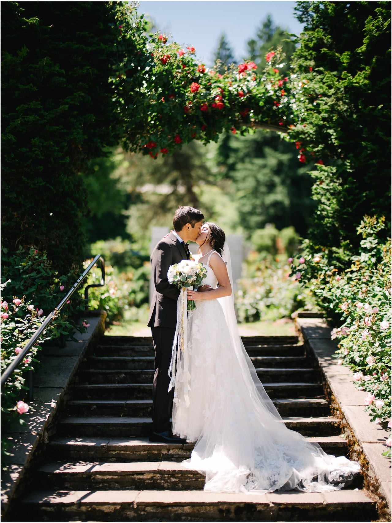  Bride and groom kiss on steps under rose arch at rose test garden 