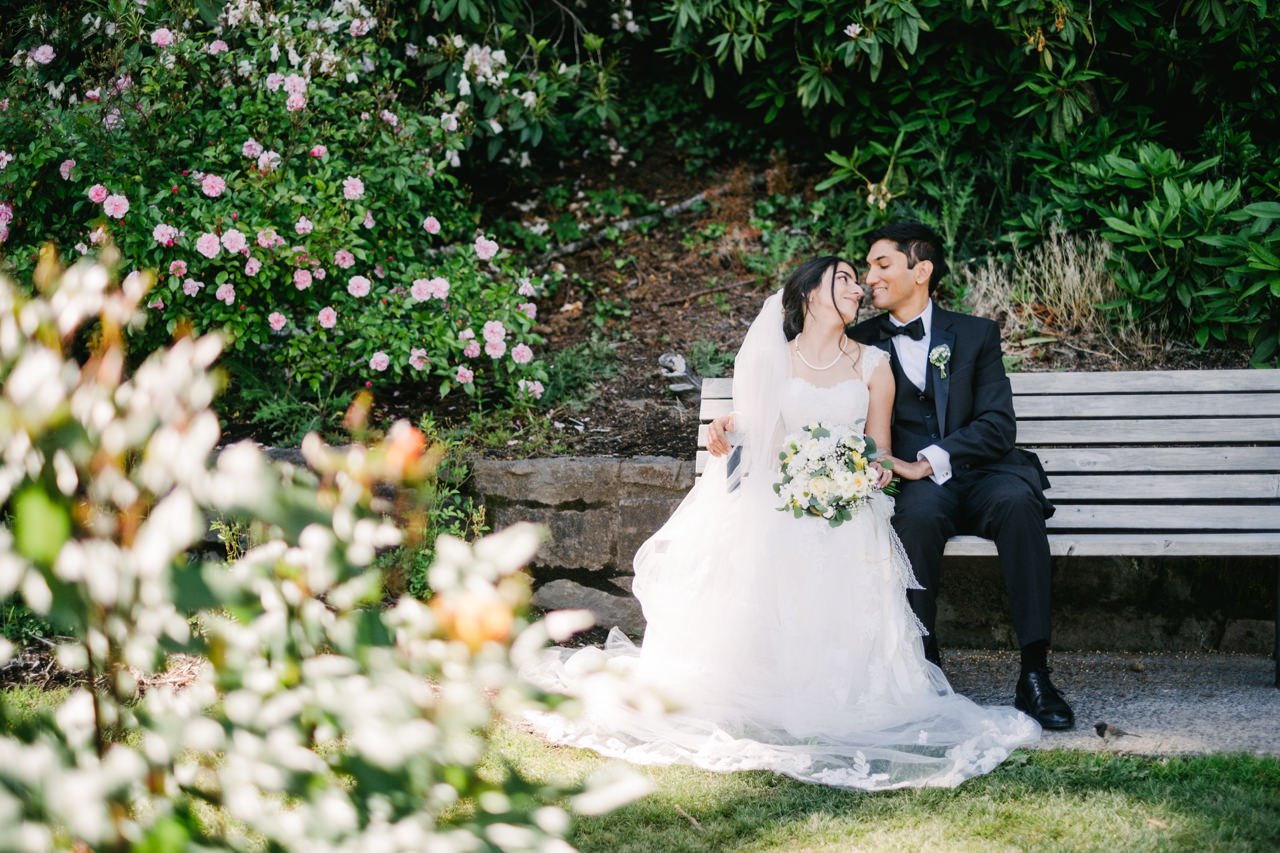  Groom and bride share intimate glance on park bench at rose garden 