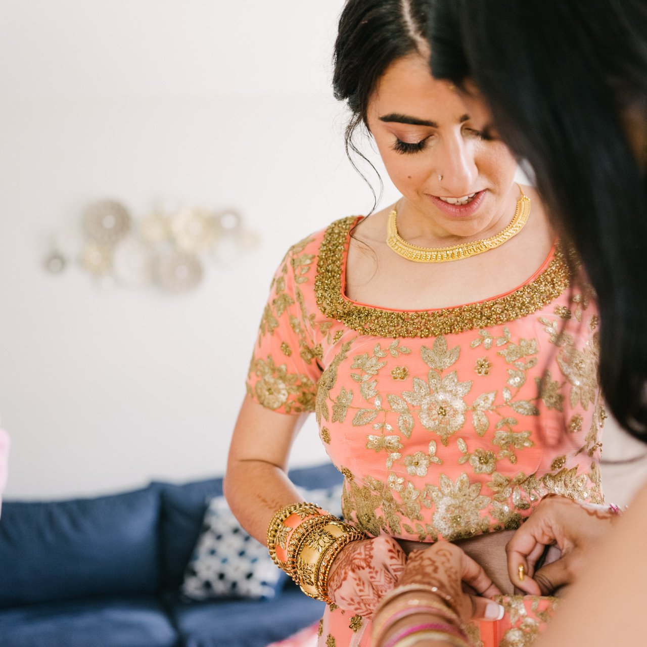  Bride in gold necklace and orange sweet sari adjusts waistline 