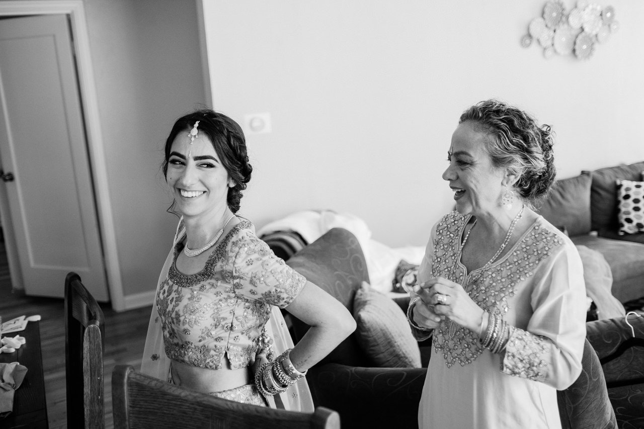  Bride laughs with mother while adjusting sari 