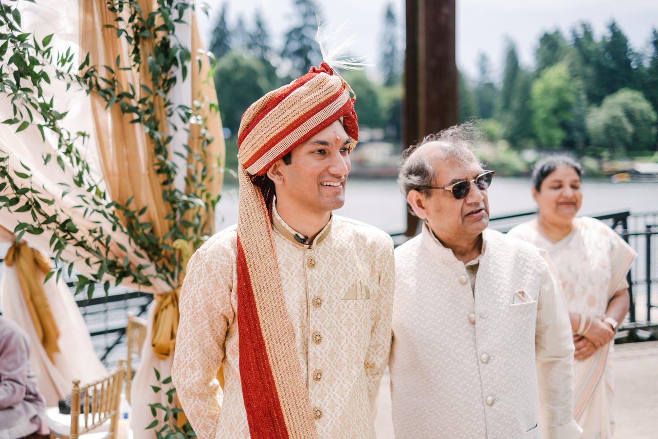  Groom in red and gold turban smiles while bride approaches 