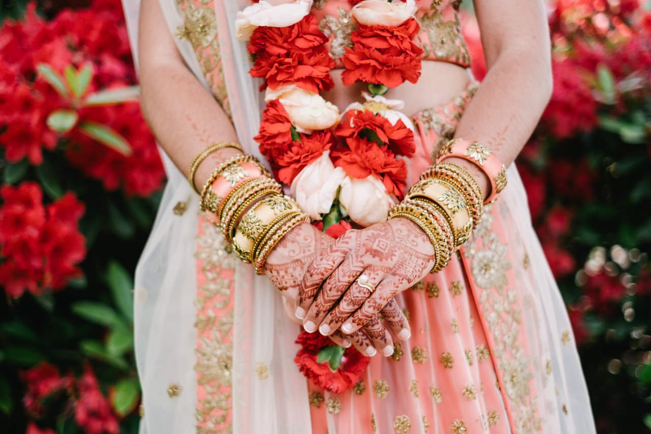  Close up photo of gold bangles and red and white garland on Indian bride 