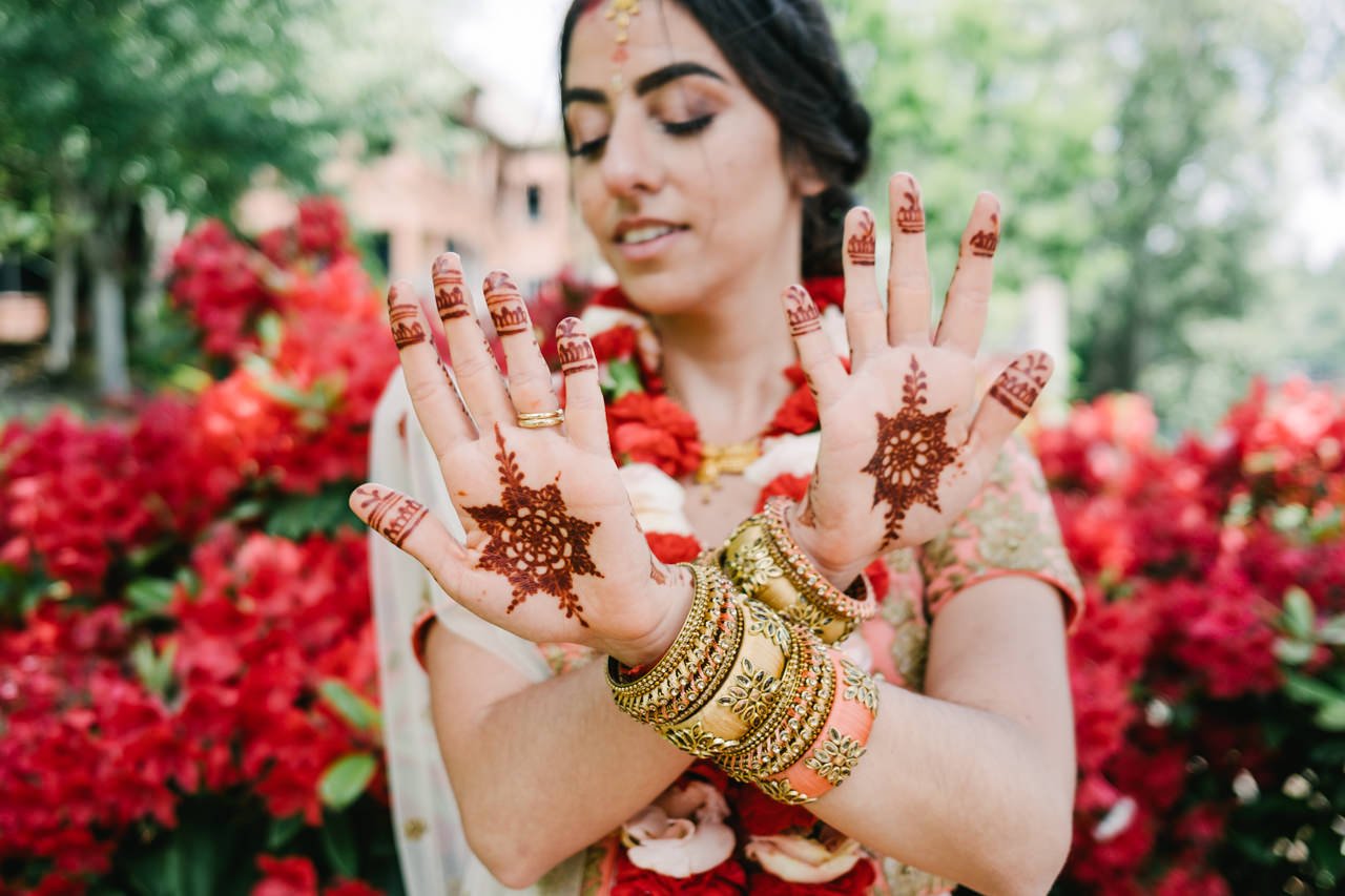  Henna designs on brides hands with red rhododendron flowers behind her 