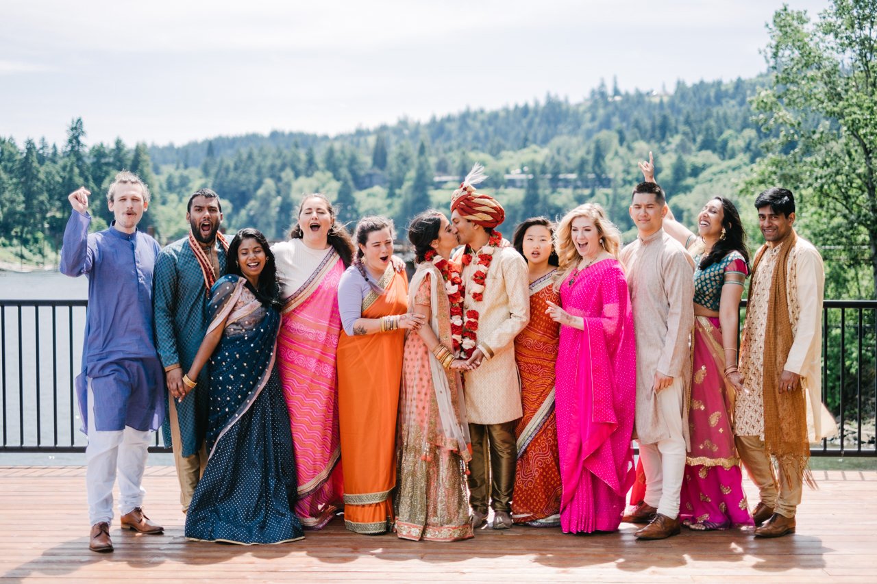  Colorful wedding party cheers as bride and groom dressed in traditional Indian attire kiss 