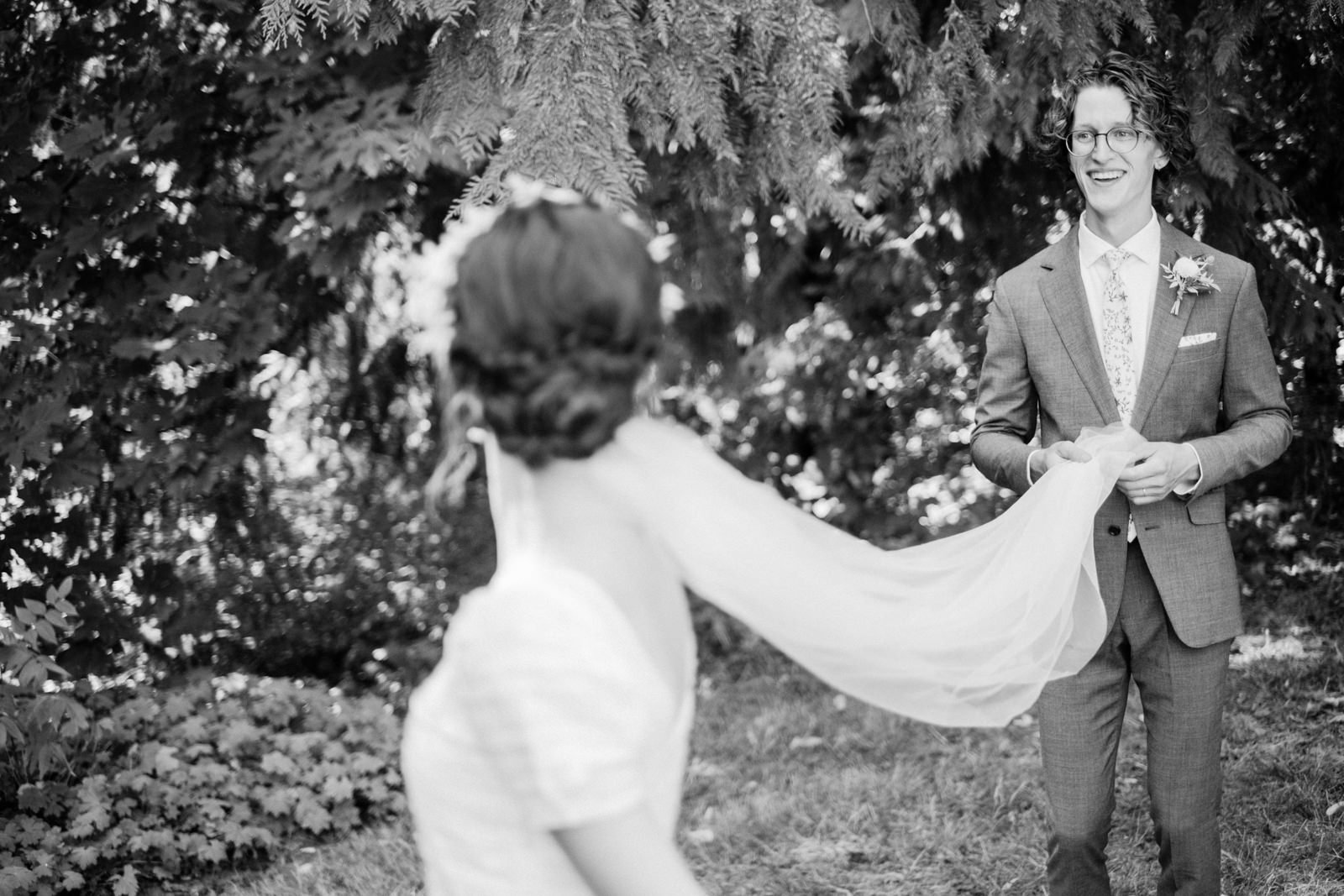  Groom laughs while holding extended long veil in black and white photo 