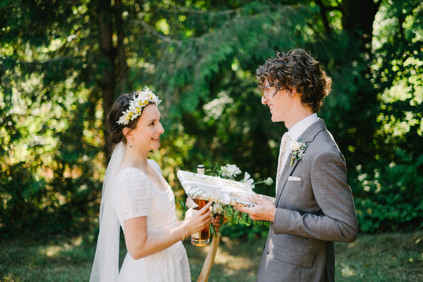  Bride with flower crown and groom in Green suit smile at each other while exchanging gifts 