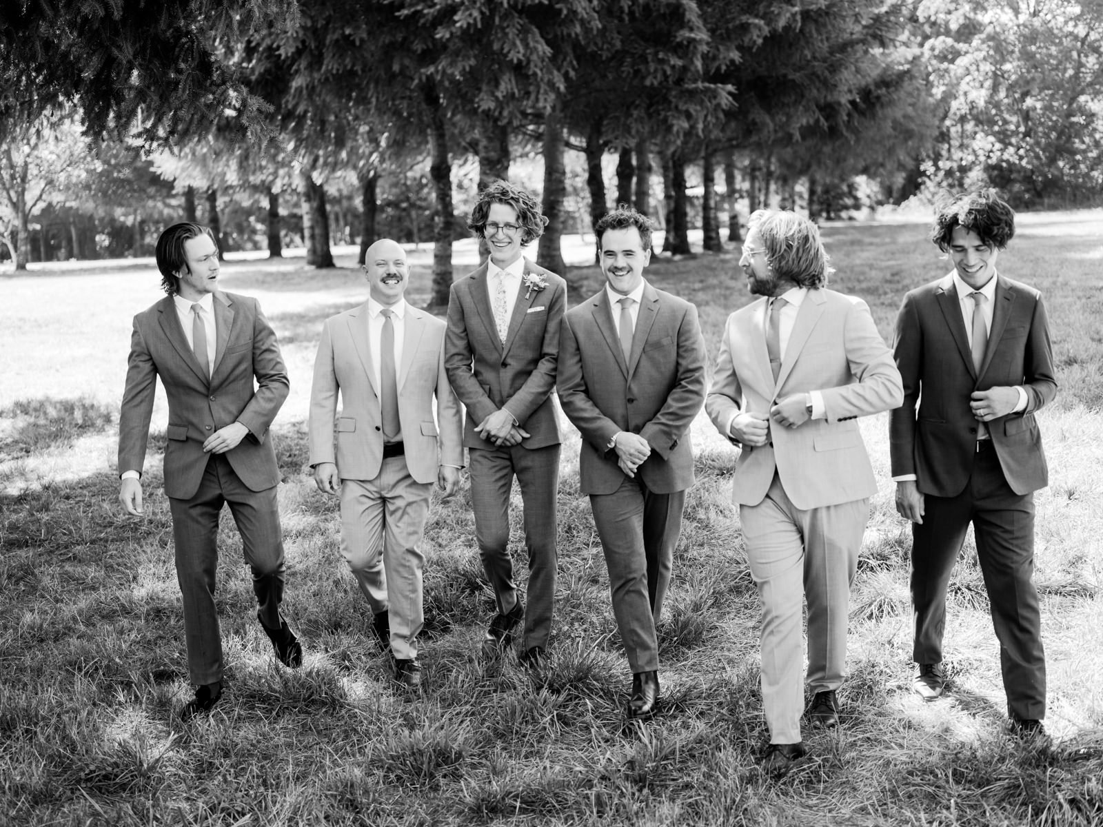  Black and white candid photo of groomsmen walking with groom with curly hair 