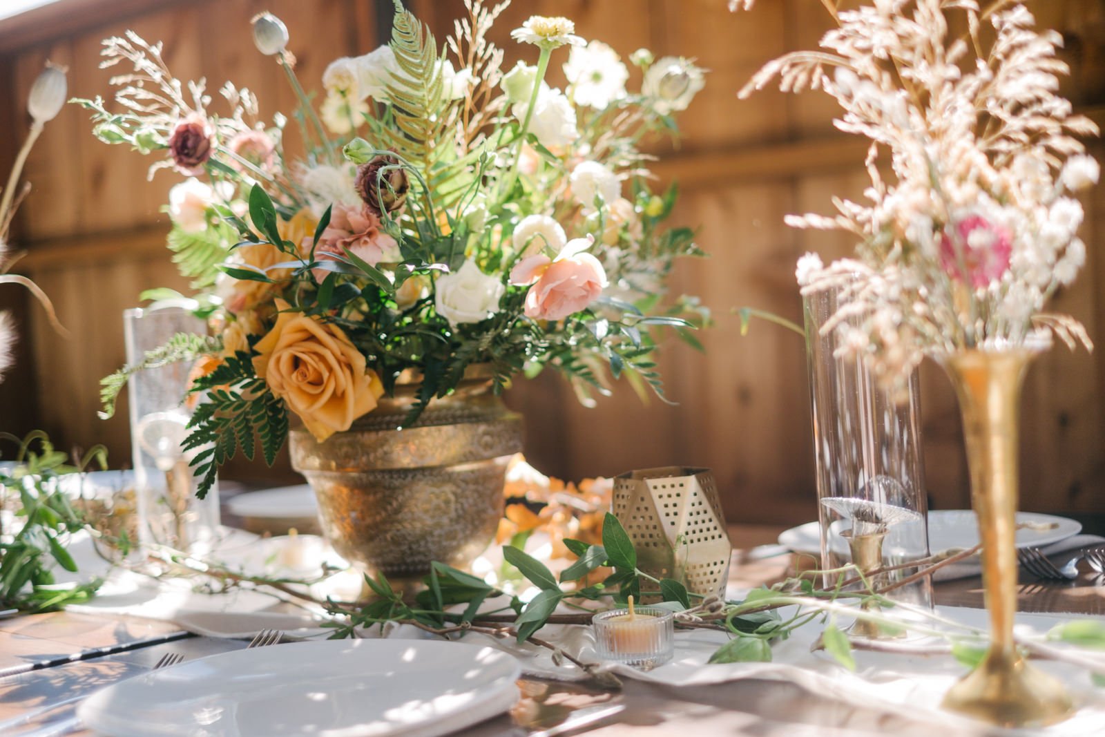  Gold vase and dried grasses with green and orange florals on dining tables 