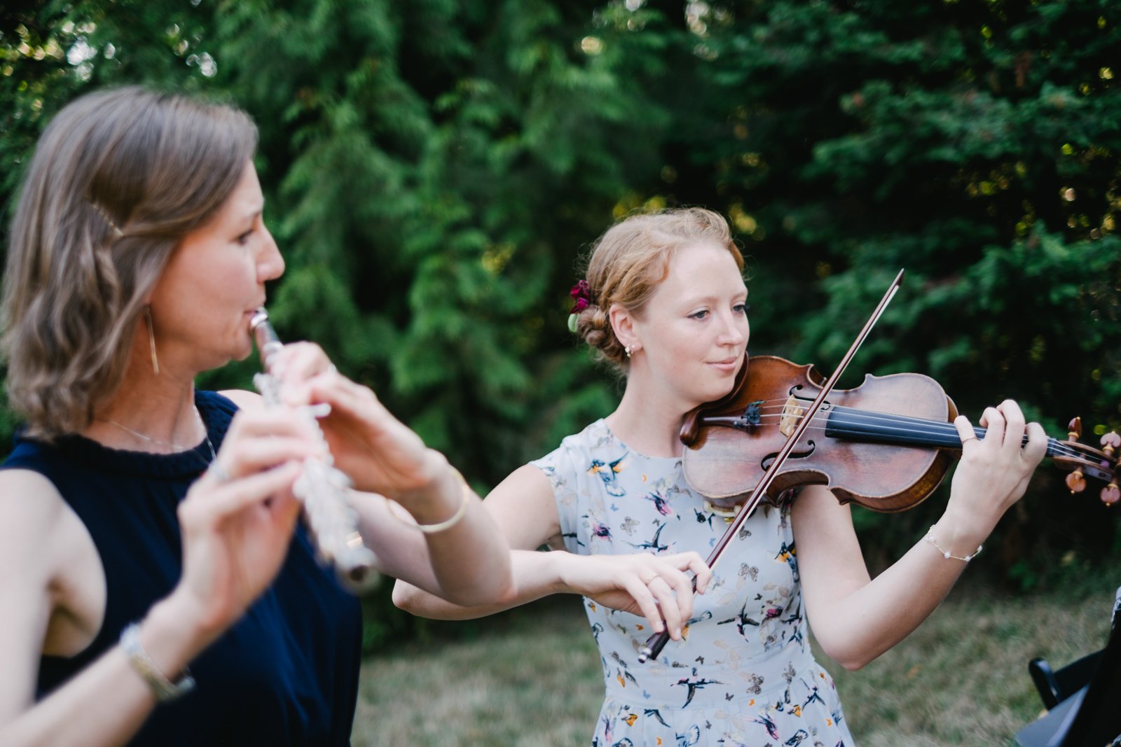  Violinist and flute player play in shade for wedding ceremony 
