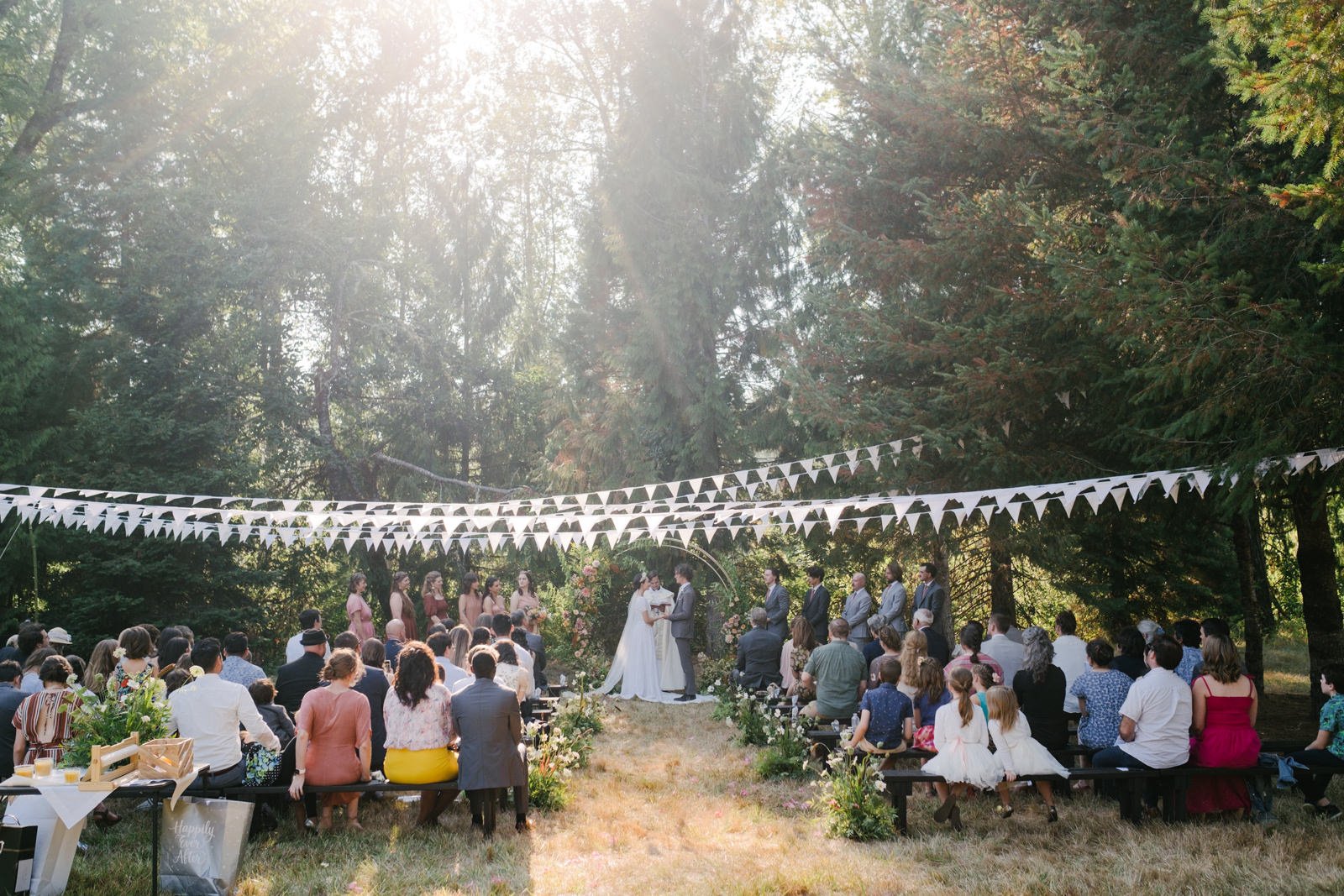  Sunlight shining on wedding ceremony in field with white flags above the guests 