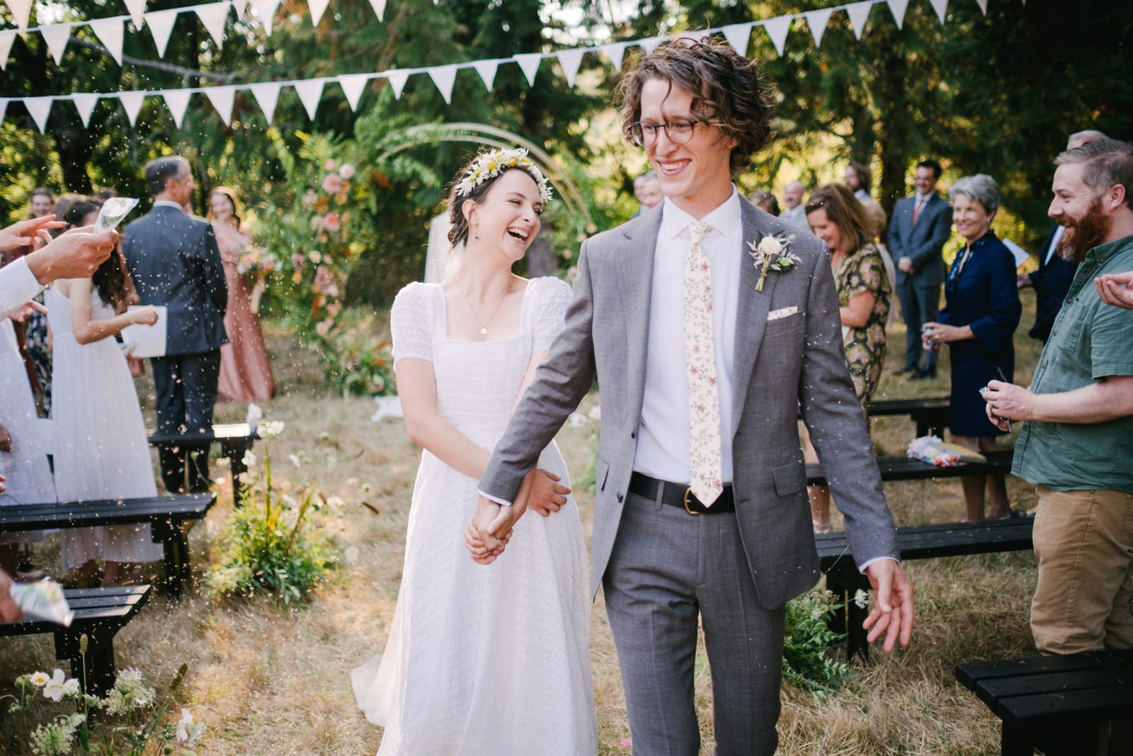  Bride and groom laugh while exiting ceremony with lavender tossed around them below white triangle flags 