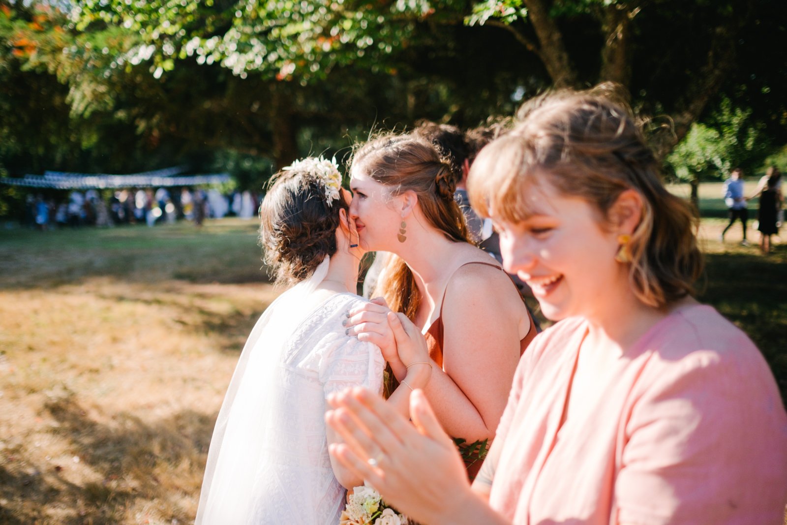  Bridesmaid kisses bride in celebration in sunshine 