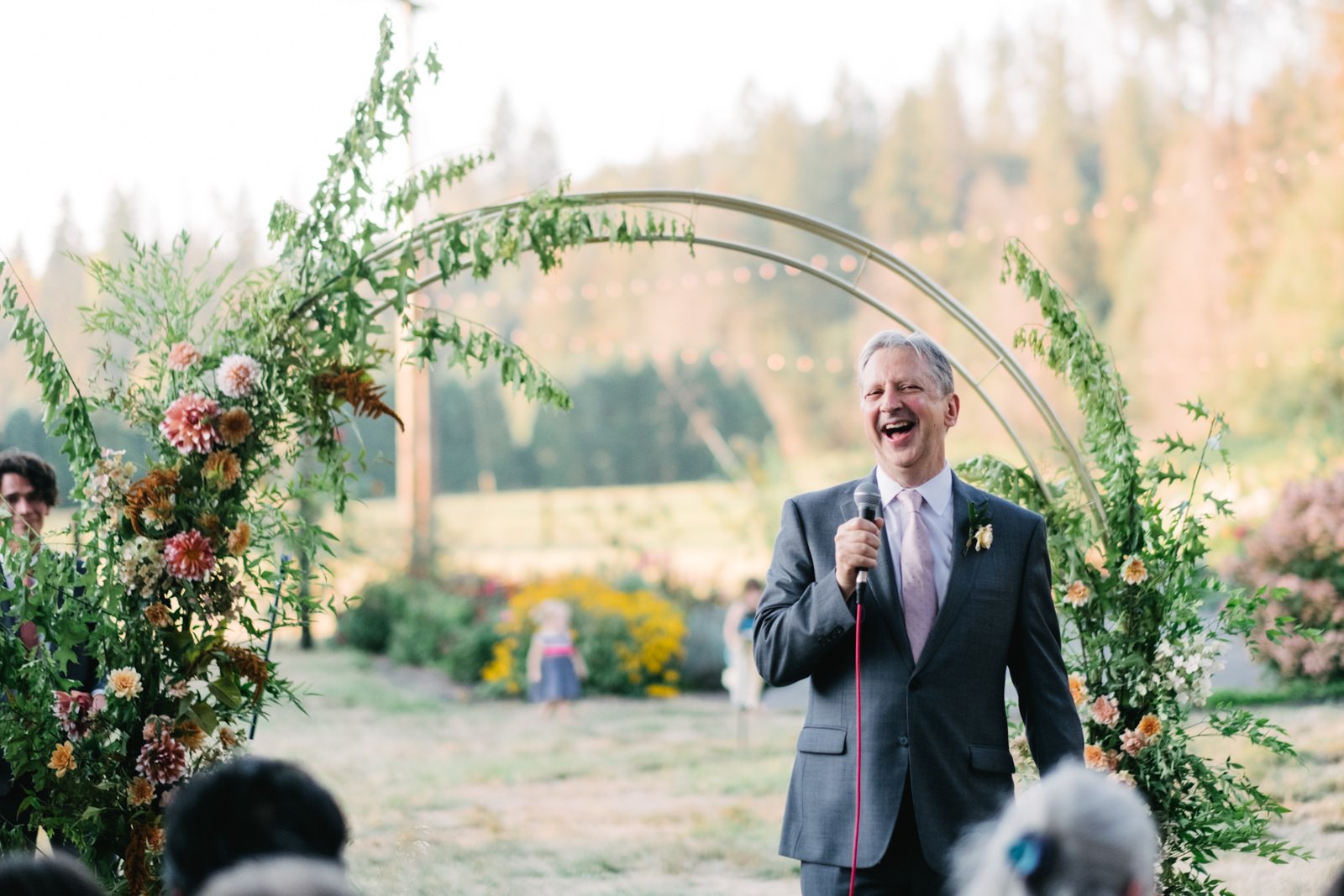  Father of bride toasts in front of floral arch in late evening 