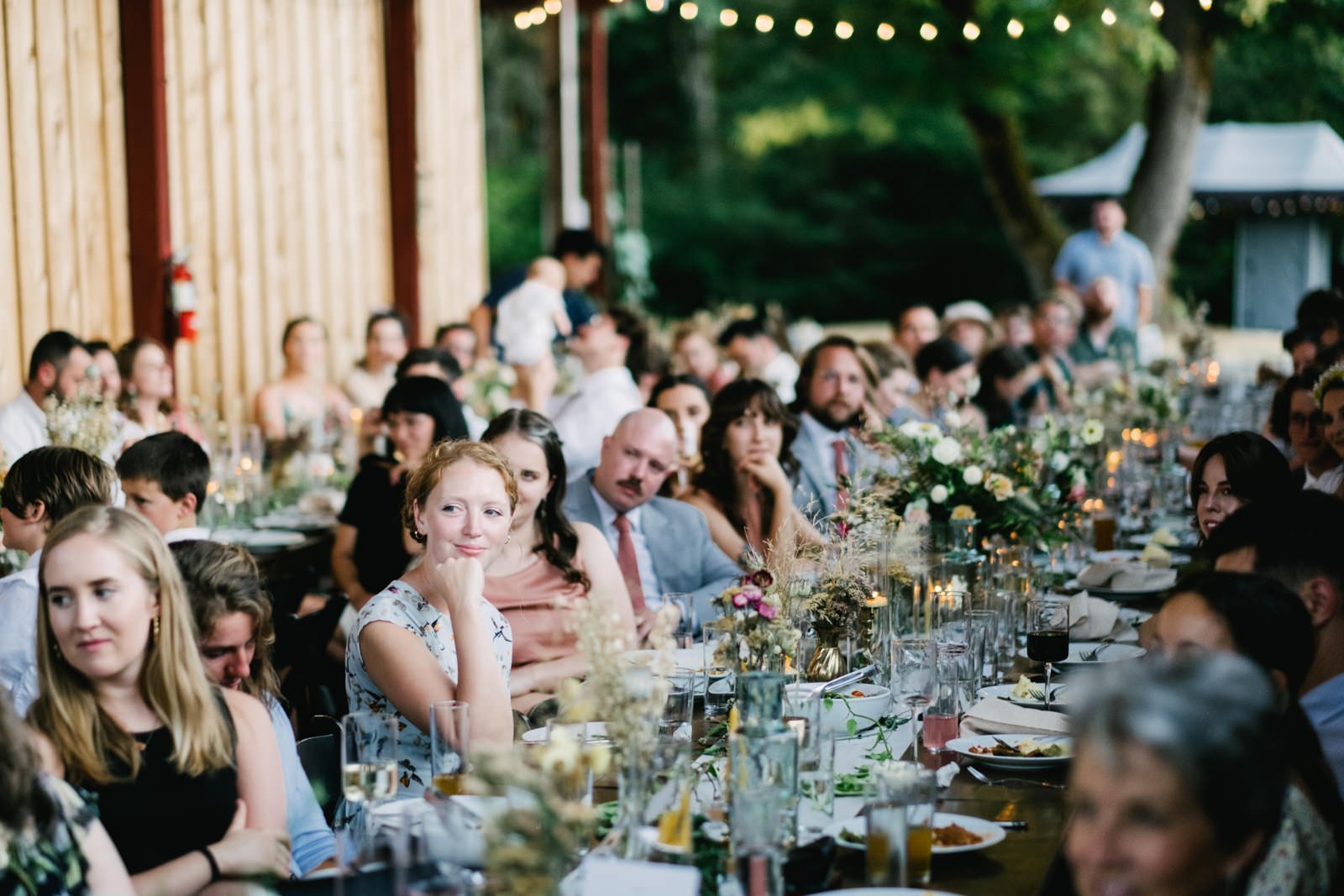  Wedding guests listen to toasts in outdoor seating area 