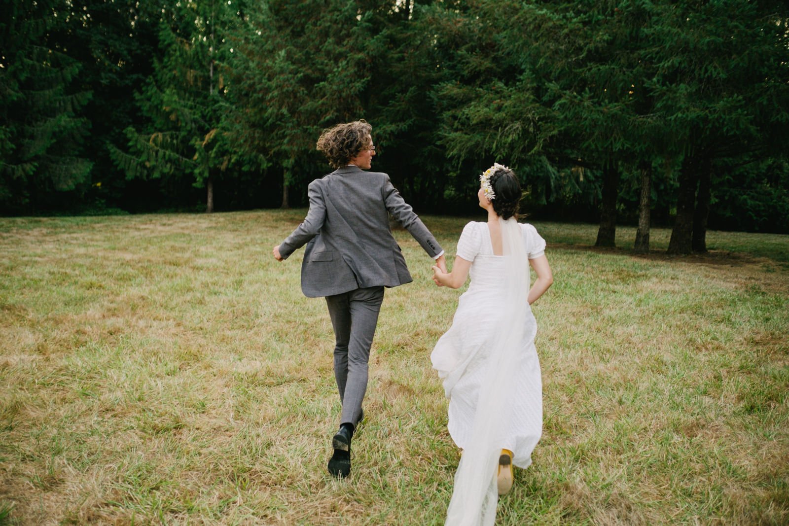  Bride and groom run away towards trees holding hands 