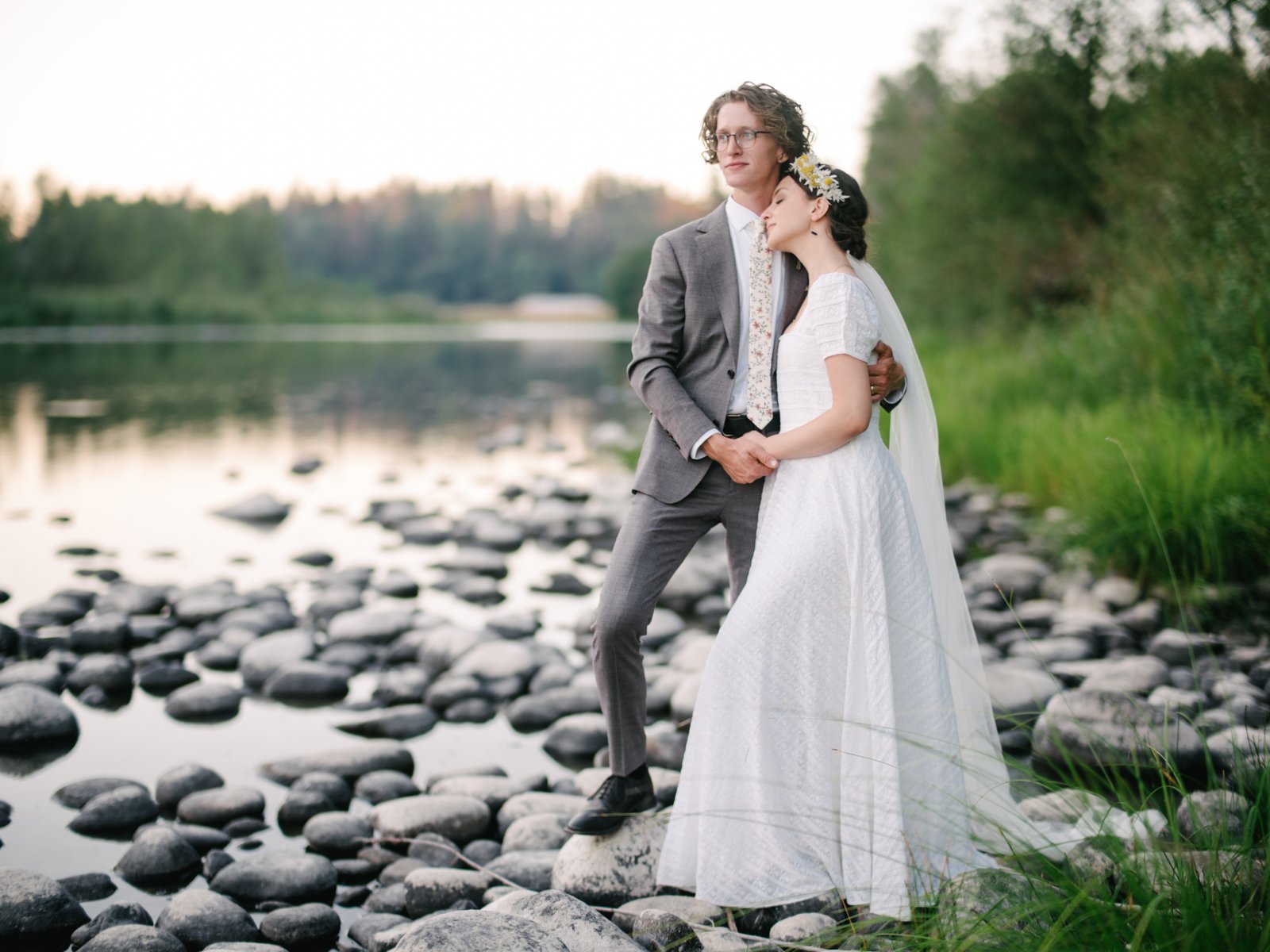  Bride and groom rest together by river bank at late sunset 