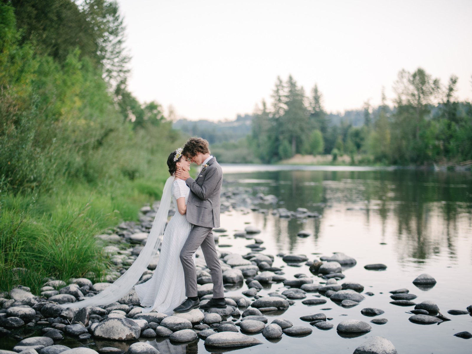  Groom holds bride head in close embrace by sunset riverbank 