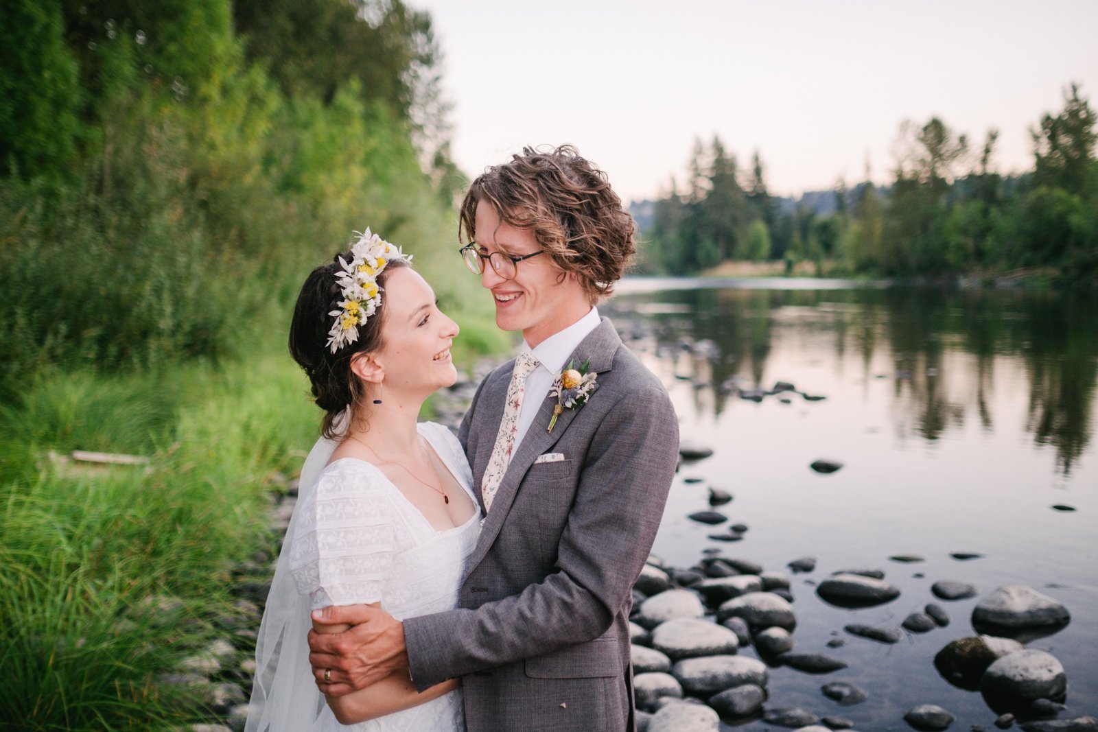  Bride and groom laugh together by river at late sunset 